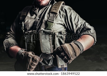 Soldier in tactical outfit and gloves putting on protective armor vest. 