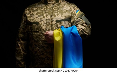 a soldier of the Ukrainian armed forces stands with a blue-yellow flag of Ukraine on a black background. Honoring veterans and commemorating those killed in the war - Shutterstock ID 2103770204