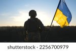 Soldier of ukrainian army holding waving flag of Ukraine against background sunset. Man in military uniform and helmet lifted up flag. Victory against russian aggression. Invasion resistance concept.