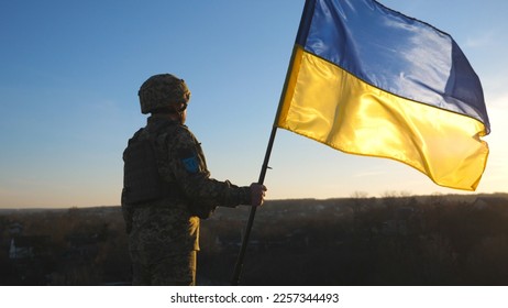 Soldier of ukrainian army holding waving flag of Ukraine against background sunset. Man in military uniform and helmet lifted up flag. Victory against russian aggression. Invasion resistance concept. - Powered by Shutterstock