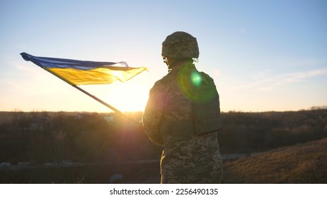 Soldier of ukrainian army runs to the hill top to wave flag of Ukraine. Man in military uniform lifted up flag against sunset as sign of victory against russian aggression. Invasion resistance. - Powered by Shutterstock