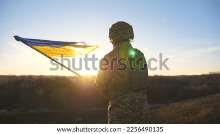 Soldier of ukrainian army runs to the hill top to wave flag of Ukraine. Man in military uniform lifted up flag against sunset as sign of victory against russian aggression. Invasion resistance.