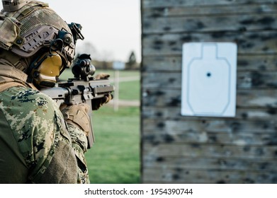 Soldier In The Uniform (Cropat Woodland Pattern) Taking Aim At The Target On The Shooting Range With His Personal Weapon. He Is Wearing Ballistic Helmet And Plate Carrier In Coyote Brown.