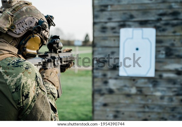 Soldier in the uniform (Cropat woodland pattern)\
taking aim at the target on the shooting range with his personal\
weapon. He is wearing ballistic helmet and plate carrier in coyote\
brown.