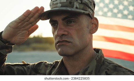Soldado uniformado parado en la atención al lado de la bandera estadounidense