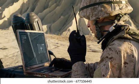 Soldier is Using Laptop Computer for Tracking the Target and Radio for Communication During Military Operation in the Desert