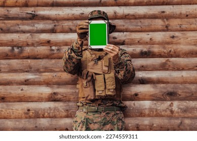 Soldier using tablet computer against old wooden wall in military camp to stay in contact with friends and family