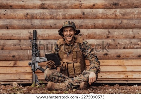 Soldier using tablet computer against old wooden wall in military camp to stay in contact with friends and family