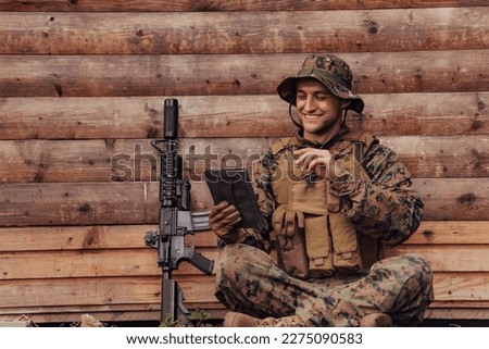 Soldier using tablet computer against old wooden wall in military camp to stay in contact with friends and family