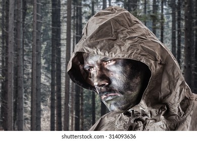 A Soldier Wearing A Poncho O Raincoat And Army Camouflage Face Paint In A Dark Wood Or Forest