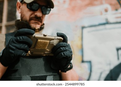 Soldier wearing tactical gloves and vest, uses a ruggedized mobile phone in an urban setting with graffiti in the background, showcasing the integration of technology in modern warfare - Powered by Shutterstock