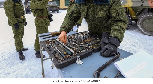 Soldiers evaluate and organize various tools on a table while performing maintenance tasks in a snowy environment. - Powered by Shutterstock