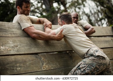 Soldiers helping man to climb wooden wall in boot camp