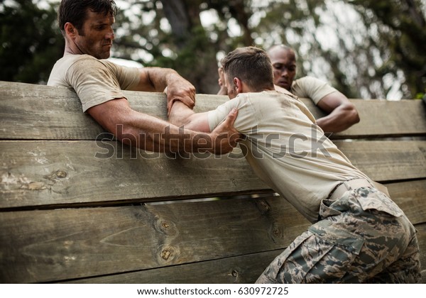 Soldiers\
helping man to climb wooden wall in boot\
camp