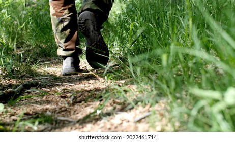 Soldier's Male Legs In Army Boots Walk On The Ground. Man In Khaki Pants. Walk Along An Earthy Path In The Forest Between Green Grass. Tourist On A Hike. Active Lifestyle. Walking