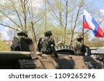 The soldiers are standing in the open hatches of the tank. The Russian military on military equipment is going around the city.