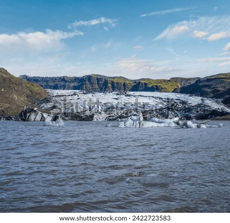 Solheimajokull glacier in southern Iceland. The tongue of this glacier slides from the volcano Katla. Beautiful glacial lake lagoon with ice blocks and surrounding mountains. People unrecognizable.
