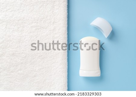 Solid antiperspirant deodorant on a blue background and white bath towel with copy space. Personal hygiene items, body care and toiletries concept. Cosmetic product to reduce perspiration. Close-up.
