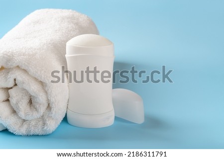 Solid antiperspirant deodorant and rolled bath towel on a blue background. Personal hygiene items, body care, toiletries concepts. Cosmetic product to reduce perspiration. Copy space. Front view.
