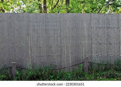 Solid blank weathered gray board fence with chain and posts in front and trees in back.