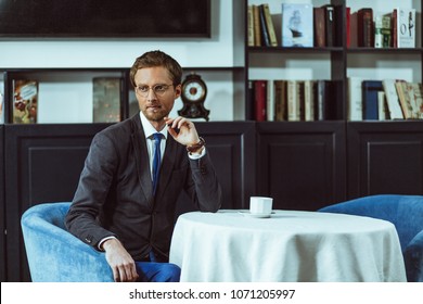 Solid businessman sitting at table at restaurant and having coffee. Looking thoughtful.