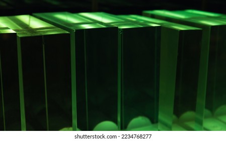Solid glass blocks stand in a row in a dark room with green illumination, abstract optic background