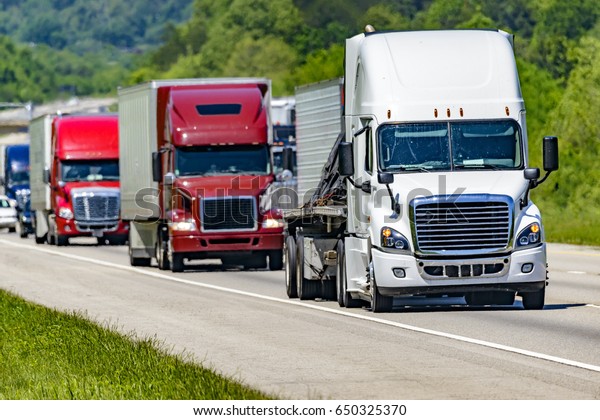 A solid line of eighteen-wheelers barrel down an\
interstate highway in Tennessee.  Heat waves rising from the\
pavement give a nice shimmering effect to vehicles and trees behind\
the lead truck.