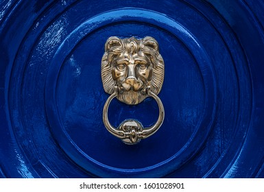 Solid metal heavy classical lion head door knocker on a deep blue painted traditional seamless door.