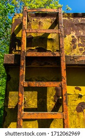 A solid metal ladder leading to the top of a construction container.  The building unit is old, weathered and covered in rust.  The peeling paint work is brown, red and yellow.