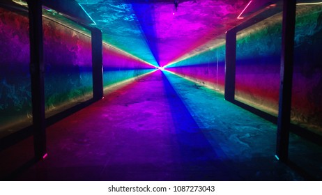 Solid rainbow laser light tunnel shines through an empty nightclub past four silhouetted columns. Alpha matte background.