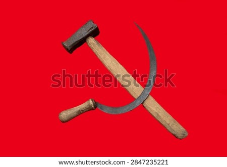 Solid red background features crossed hammer and sickle symbol. Rustic wooden handles meet metallic heads. Represents collective labor and agricultural unity historically