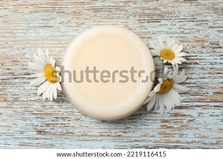 Solid shampoo bar and chamomiles on light wooden table, flat lay. Hair care