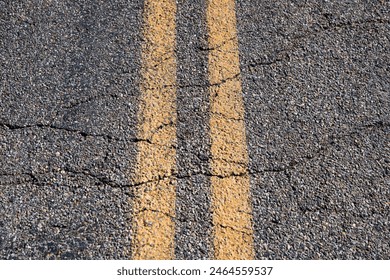 Solid yellow lines on road in broken asphalt on desert highway.  
