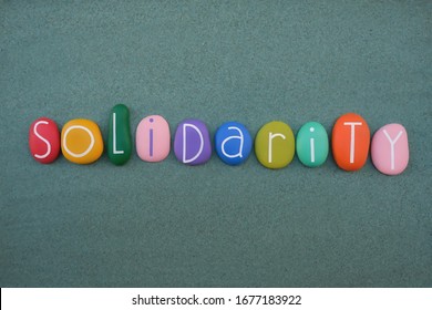 Solidarity word composed with multi colored stone letters over green sand