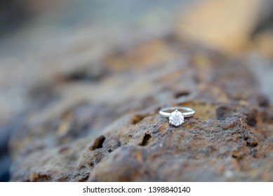 Solitaire diamond ring on copper colored stone rock at a park.