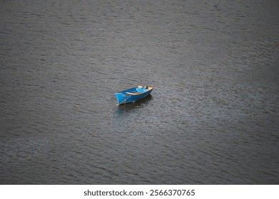 A solitary blue boat floats on calm rippling water, creating a peaceful and minimalistic scene of tranquility. - Powered by Shutterstock