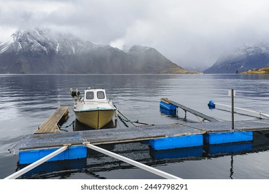 A solitary boat tied to a jetty, with tranquil waters and foggy mountains in the backdrop. - Powered by Shutterstock