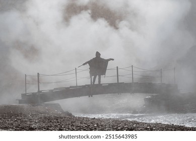 Solitary Figure on Misty Suspension Bridge Over Rocky Ravine - Powered by Shutterstock