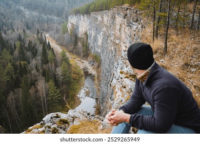 A solitary figure sits quietly on a steep cliff, lost in deep contemplation, gazing intently at the sprawling, autumncolored valley that lies below, embraced by natures serenity - Powered by Shutterstock