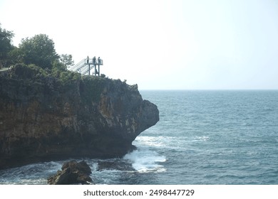 A solitary figure stands on a viewing platform, taking in the breathtaking view of the ocean. The cliffside offers a dramatic backdrop to this peaceful scene - Powered by Shutterstock