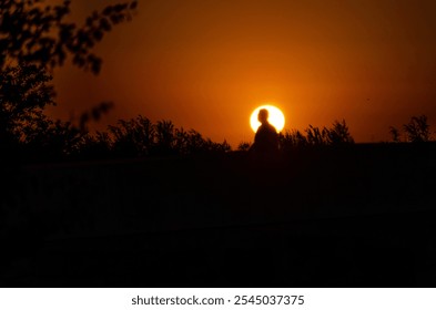 A solitary figure stands silhouetted against a vibrant orange sunset. The dramatic contrast between the dark figure and the fiery sky creates a sense of peace and tranquility. - Powered by Shutterstock