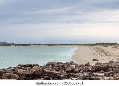 A solitary figure strolls along the expansive sandy beach of Gurteen Bay, Ireland, at sunset. The scene highlights the tranquil turquoise sea, soft sands, and a cloudy sky - Powered by Shutterstock