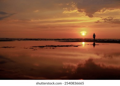 A solitary figure walks along the shore during a vibrant sunset, reflecting on the calm water. - Powered by Shutterstock