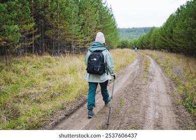 A solitary hiker meanders slowly along a peaceful forest trail, equipped with a sturdy backpack and a reliable walking stick, surrounded by vibrant, lush greenery all around - Powered by Shutterstock