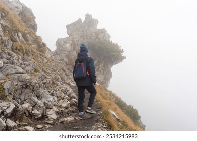 Solitary hiker navigating misty mountain trail, surrounded by rugged rocky terrain and low-hanging clouds. True adventure in challenging weather, capturing the spirit of outdoor exploration.  - Powered by Shutterstock