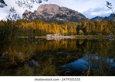 A solitary house with a prominent mountain backdrop, shot during sunset golden hour with a lake in the foreground reflecting the forests - Powered by Shutterstock