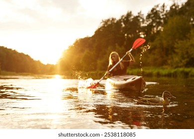 A solitary kayaker gracefully paddles through a peaceful river during a serene sunset, completely surrounded by the vibrant colors of autumn foliage that paint the landscape beautifully - Powered by Shutterstock