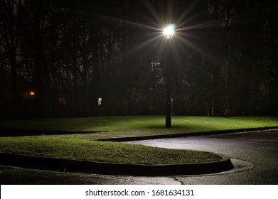 Solitary Lamp Post at Night, Illuminated, Casting Light on a Wet, Empty Parking Lot & Lawn
