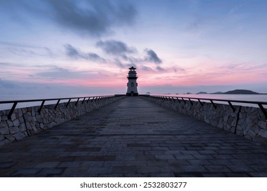 Solitary lighthouse stands on a stone pier, under a tranquil dawn sky with scattered clouds and gentle pink hues. - Powered by Shutterstock