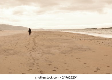 Solitary Man Taken From Behind Walking In An Empty Beach.Footprints On The Sand.